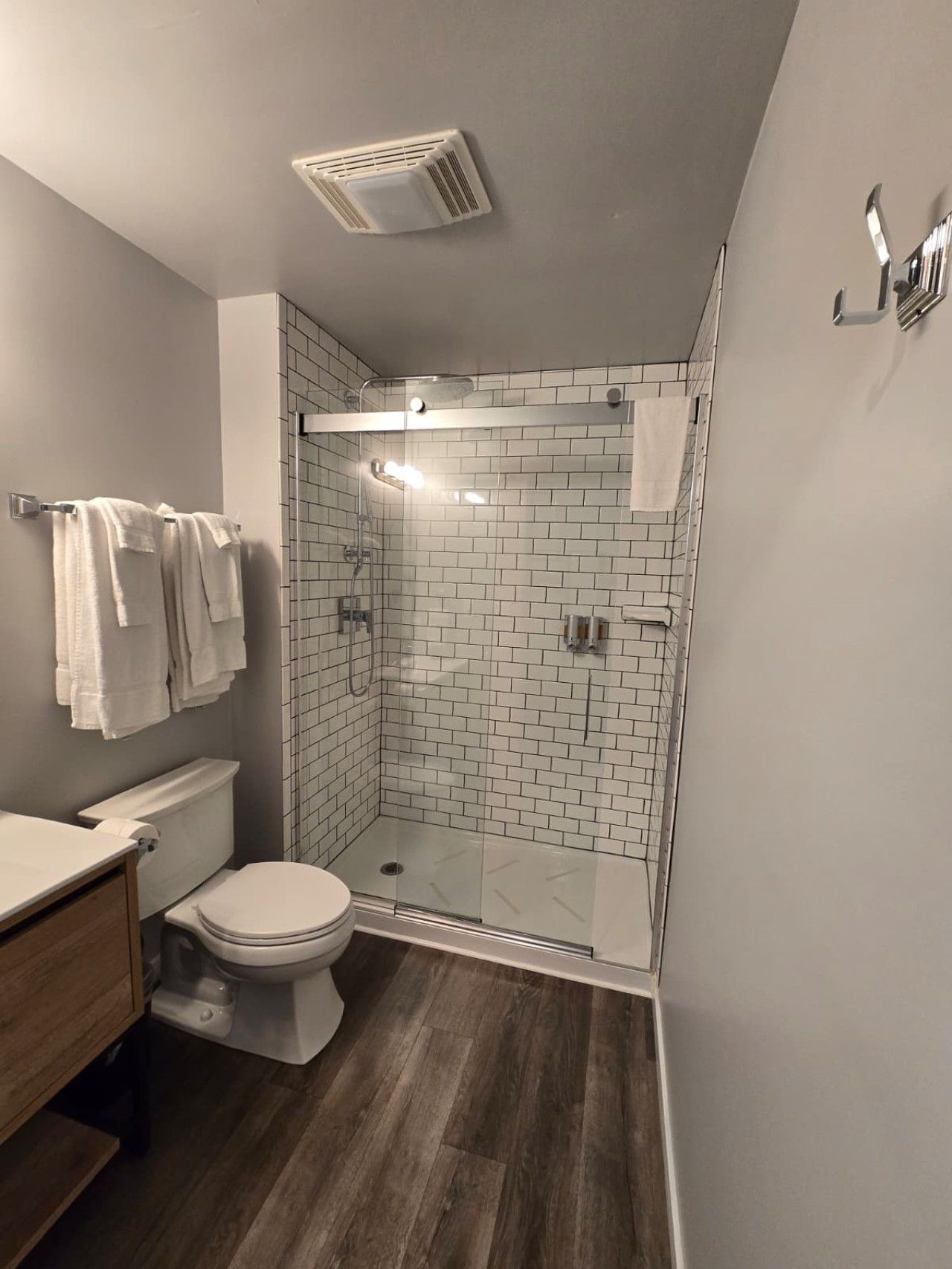 Ein modernes Badezimmer mit einer Duschkabine aus Glas, weißen Fliesenwänden, einem Holzwaschtisch und einer Toilette.