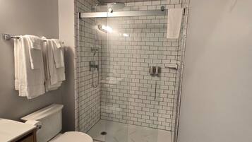 Ein modernes Badezimmer mit einer Duschkabine aus Glas, weißen Fliesenwänden, einem Holzwaschtisch und einer Toilette.