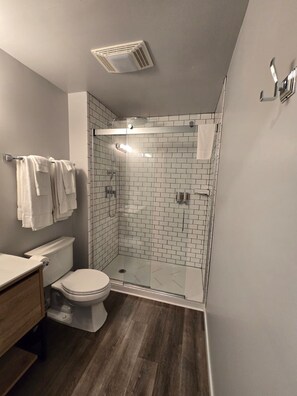 Ein modernes Badezimmer mit einer Duschkabine aus Glas, weißen Fliesenwänden, einem Holzwaschtisch und einer Toilette.