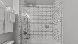 A modern bathroom with white subway tiles, a glass-enclosed shower, and a white bathtub. - Victorian Inn #117 | King Bed (Elkhart Lake)
