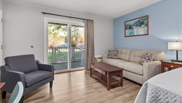 Quarto com sofá, poltrona, mesa de centro de madeira, cama e porta de vidro deslizante para uma área externa.