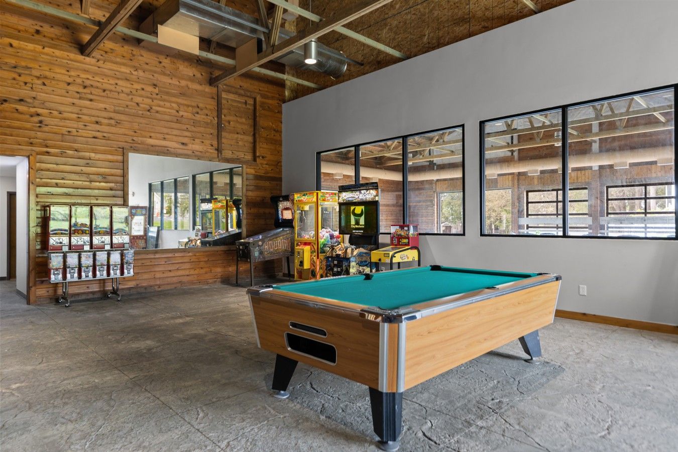 A pool table in a room with wooden walls and large windows.