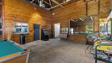 A wooden interior with a pool table, a trash bin, a vending machine, and a claw machine.