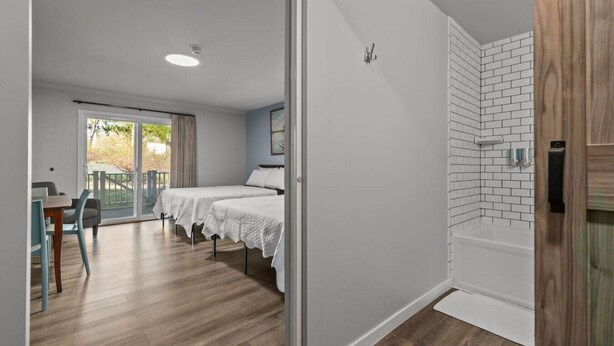 Une chambre d’hôtel avec un balcon, deux lits, un plancher en bois et un mur recouvert de carreaux blancs.