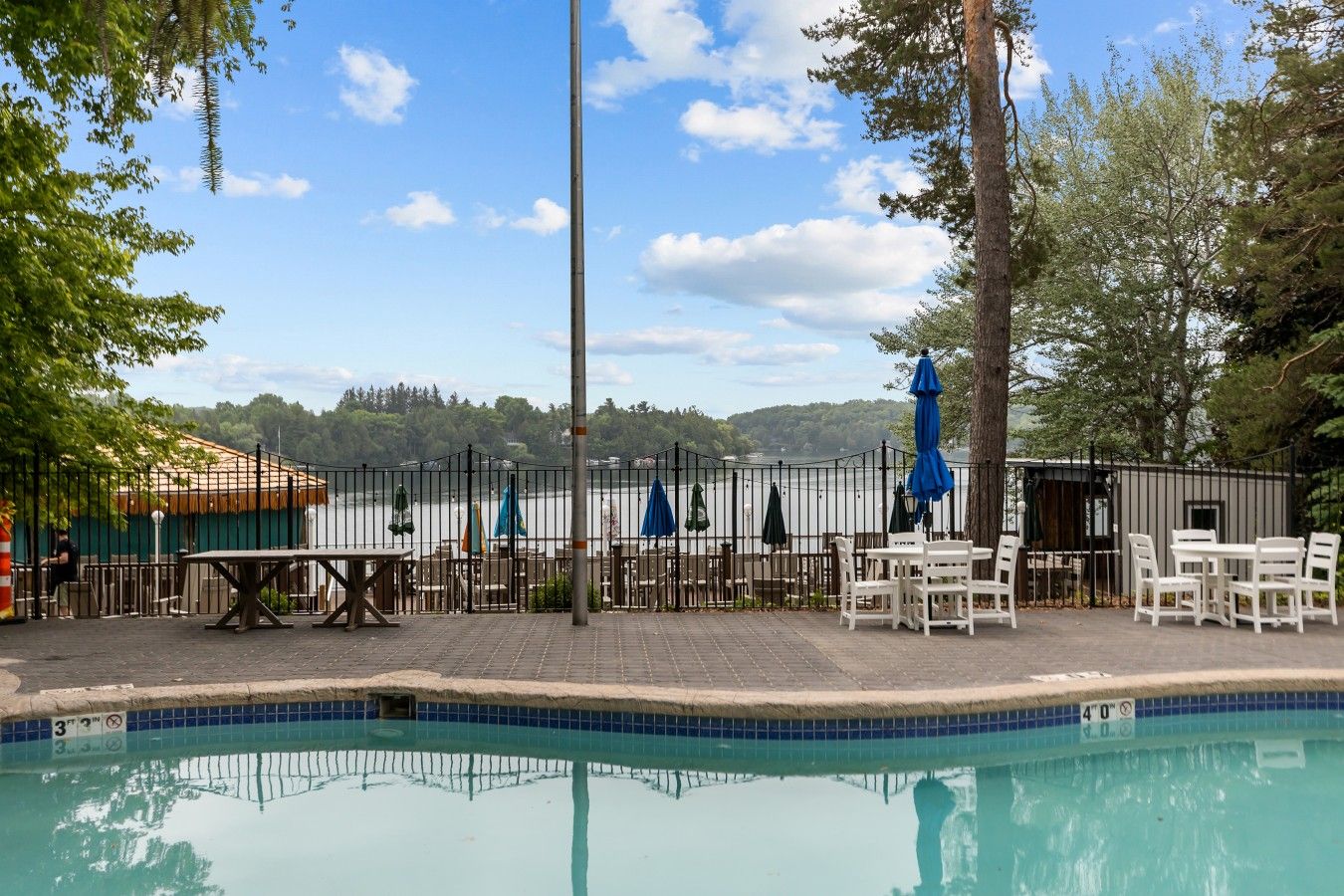 Ein Swimmingpool mit umzäuntem Deckbereich, Sitzgelegenheiten im Freien und Blick auf ein Gewässer.