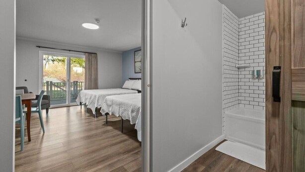 Una habitación de hotel moderna con balcón, dos camas, zona de comedor y cabina de ducha.