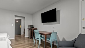 Habitación de hotel con piso de madera, un televisor montado en la pared, un escritorio pequeño con una computadora, dos sillas y un sofá.