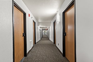 A hotel hallway with carpeted floors, wooden doors, and wall-mounted light fixtures.