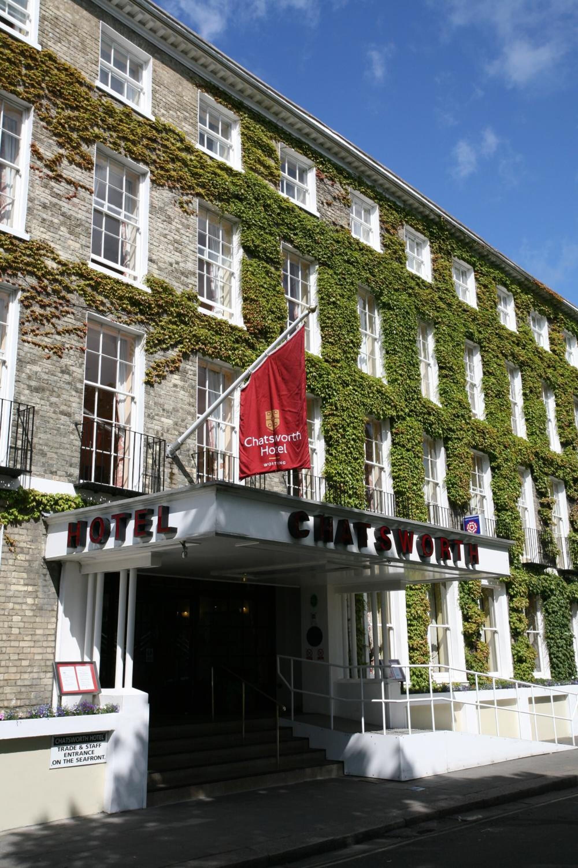 A hotel with a classic facade, ivy-covered walls, and a prominent entrance with a red flag.