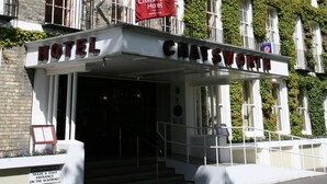 Un hotel con fachada clásica, muros cubiertos de hiedra y una entrada destacada con una bandera roja.
