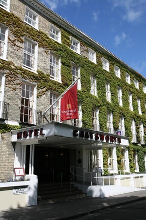 Um hotel com fachada clássica, paredes cobertas de hera e uma entrada destacada com uma bandeira vermelha.