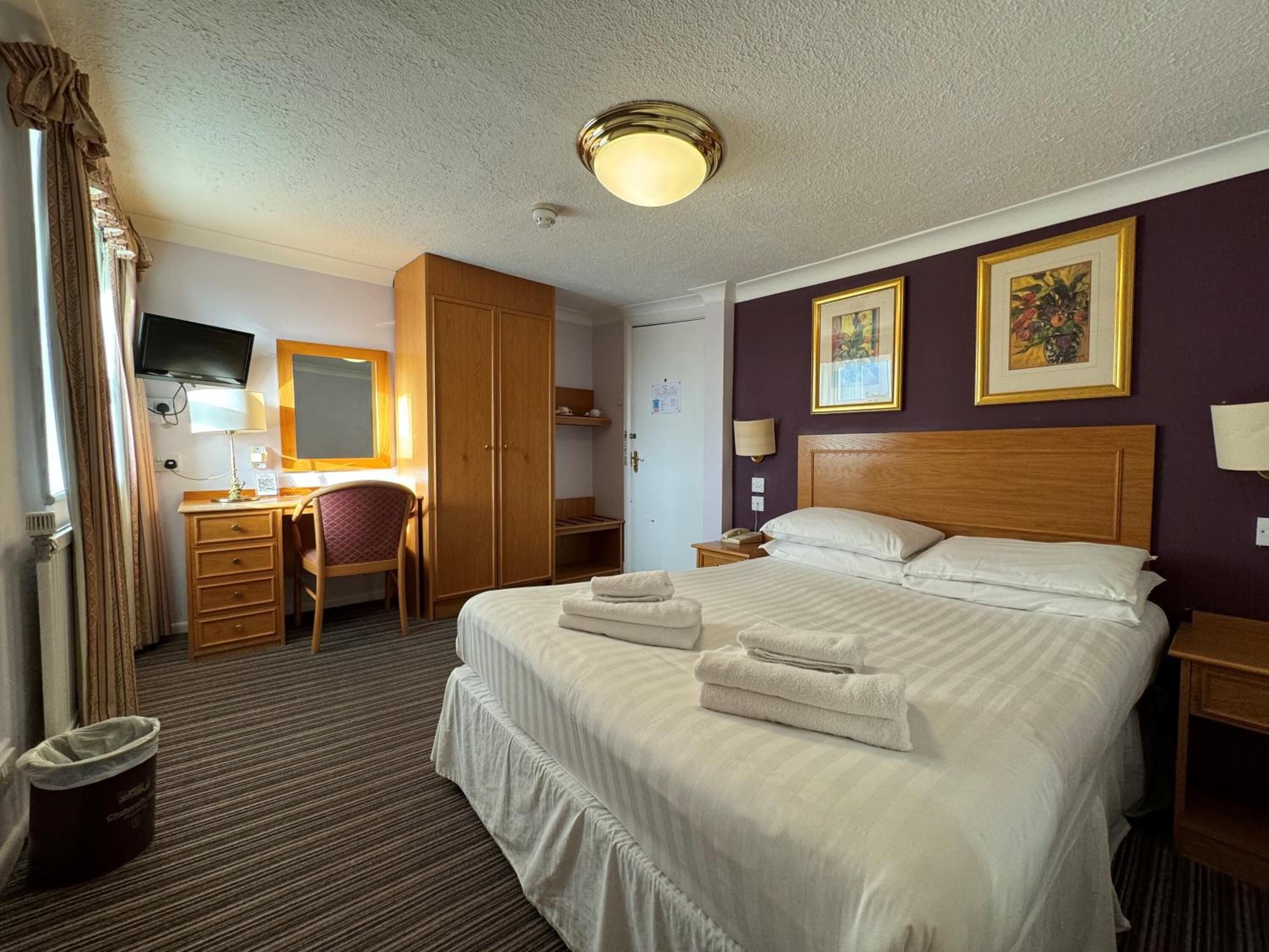 A hotel room with a bed, a desk, a chair, a wardrobe, and a television.