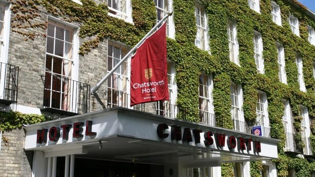 En hotelindgang med en stenfassade, et rødt flag og navnet 'CHATSWORTH HOTEL' vist.