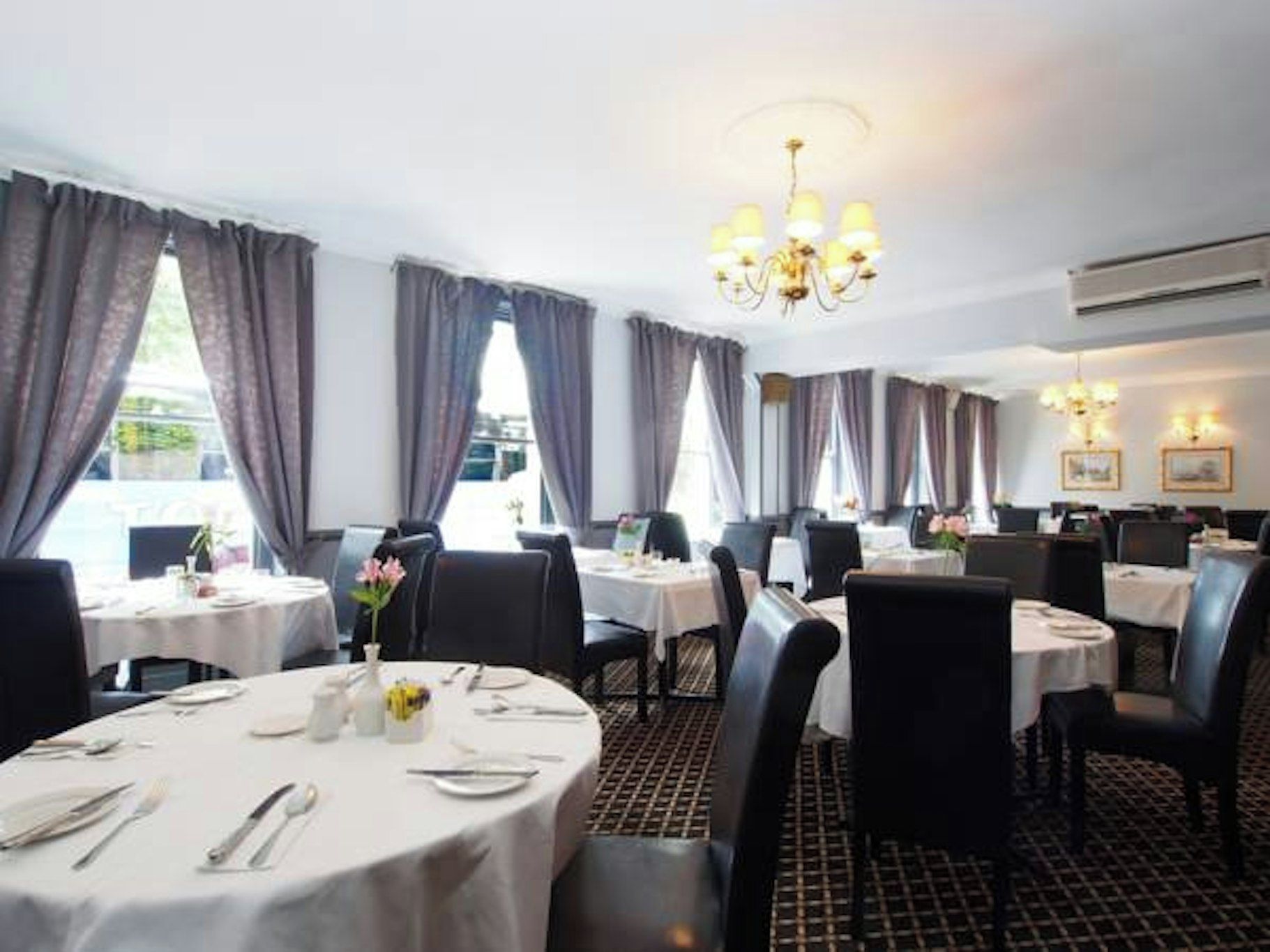 A restaurant with round tables, chairs, and a chandelier.
