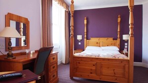 Una cama con dosel, un escritorio con lámpara, una silla y un aparador en una habitación con paredes moradas.