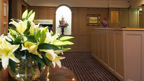 Et receptionområde med en vase blomster, en receptionsdisk, et indrammet billede og et skilt, der angiver stueetagen.