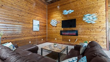 Een gezellige kamer met houten wanden, een flatscreen televisie, een open haard en lederen meubels.