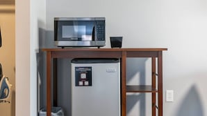 A compact kitchenette with a microwave and a small refrigerator, a wooden table above the fridge, and a QR code on the fridge door. - Victorian Inn #246 | 2 Queen Beds (Elkhart Lake)