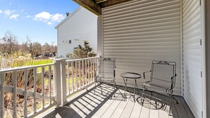 A covered porch with a white railing, two metal chairs, and a small table. - Victorian Inn #246 | 2 Queen Beds (Elkhart Lake)