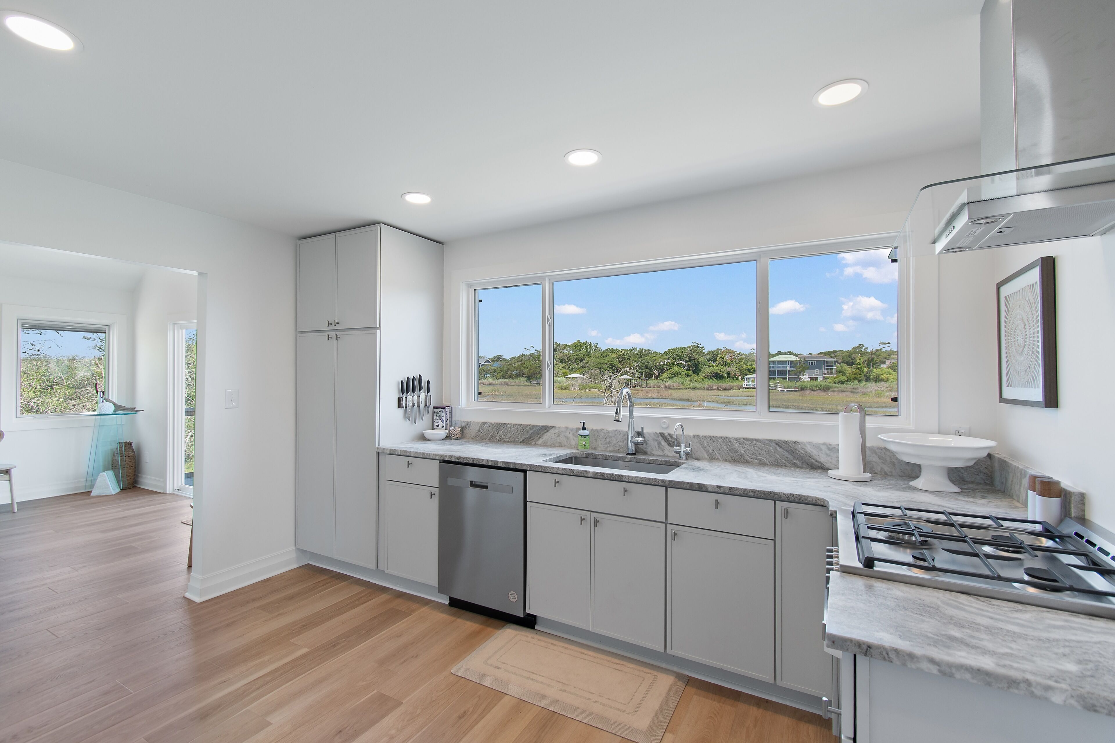 A modern kitchen with a dishwasher, sink, and stove, large windows, and a view of greenery.