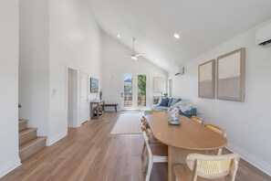 Ein geräumiges Zimmer mit einem Holzespeisetisch, Korbstühlen, einem Deckenventilator und Blick durch eine Glastür auf einen Außenbereich.