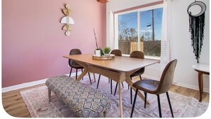 Een eetgedeelte met een houten tafel, stoelen, een hanglamp en een raam met uitzicht.