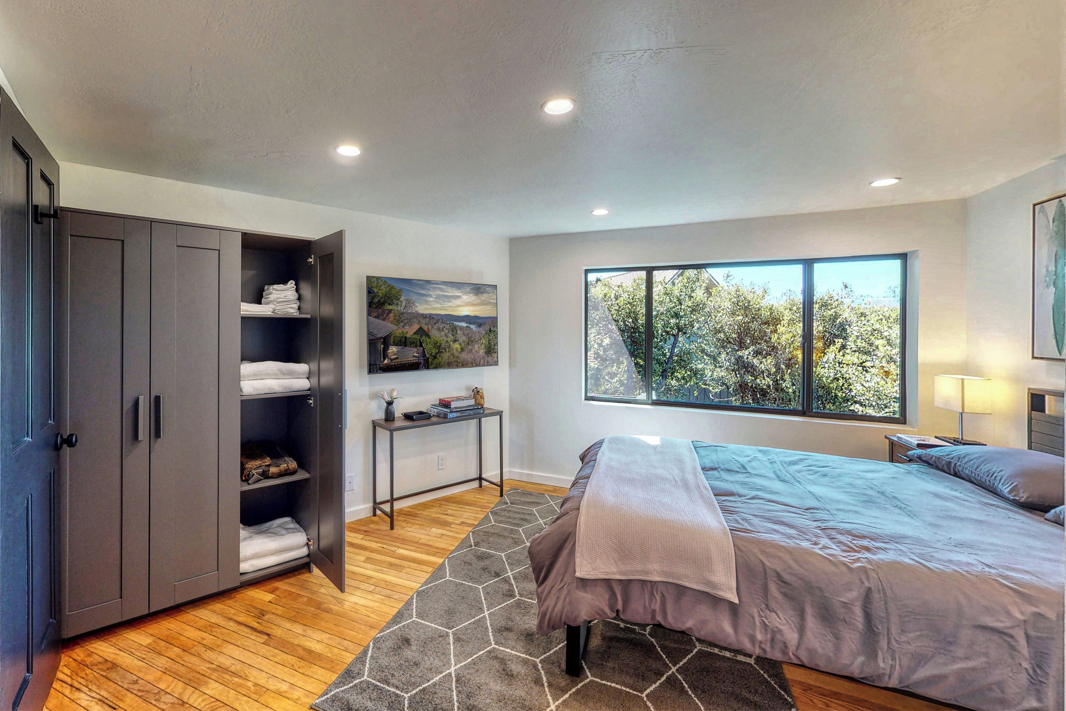 A bedroom with a bed, a wardrobe, a desk, and a window with a view.
