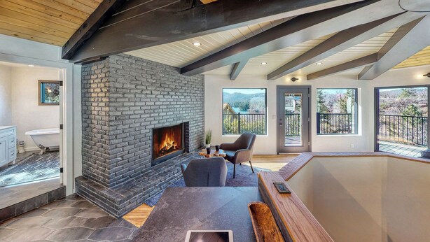 A modern interior with a stone fireplace, wooden beams, and large windows offering views. - 3-BEDROOM, 3-BATH ARCHITECTURAL MARVEL IN LAKE ARROWHEAD (Lake Arrowhead)