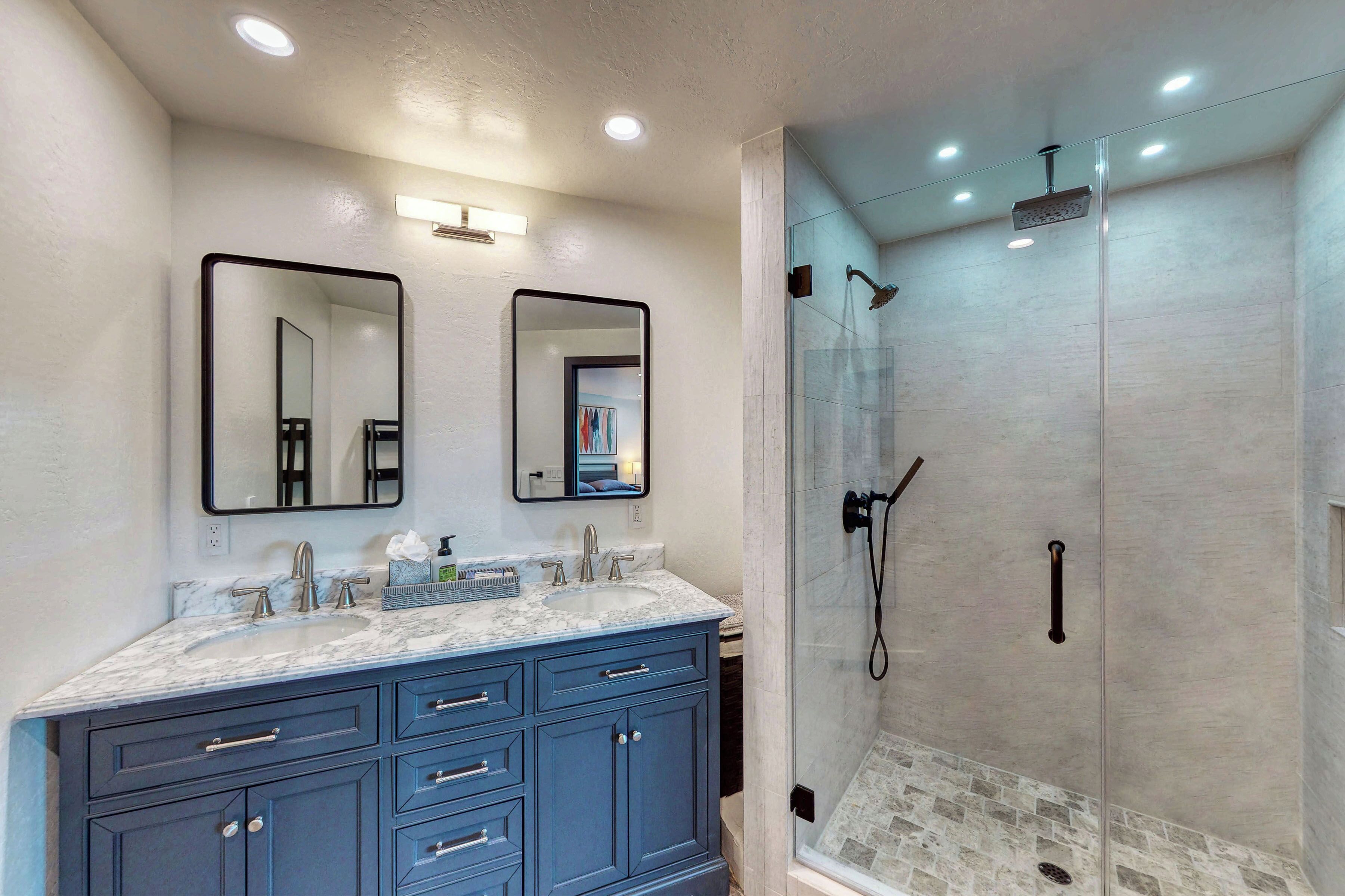 A bathroom with a marble sink, two mirrors, a glass shower enclosure, and a blue vanity.