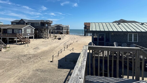 A beachfront property with multiple buildings, a sandy beach, and a clear blue sky. - Beach Dreamer with Ocean Views, 120 Steps to the Beach • Buxton, NC, OBX (Buxton)