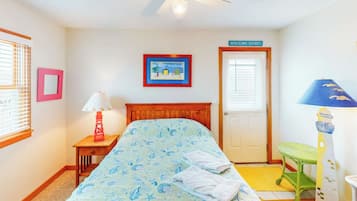 A bedroom with a bed, a nightstand, a lamp, a framed picture, a door with a sign, and a ceiling fan.