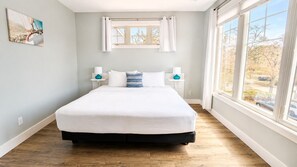 A bedroom with a bed, a window, and a painting on the wall.