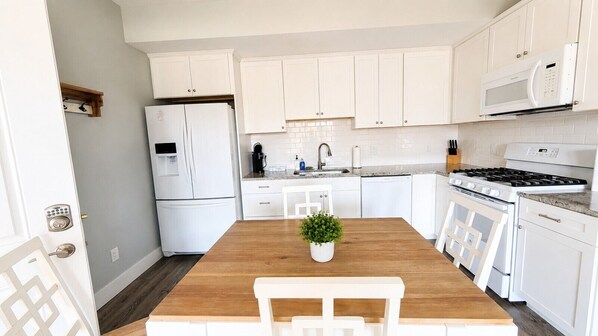 Una cocina moderna con armarios blancos, una mesa de comedor de madera y una estufa empotrada.