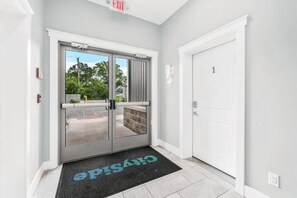 A hotel entrance with a glass door, a black mat with 'CHRISTINE' text, and a white door labeled '1'. - The Ledge 9 | 2BR | Rooftop Patio |Downtown (Traverse City)