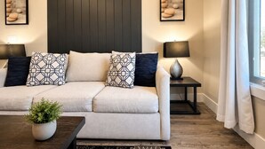Een moderne woonkamer met een bank, twee bijzettafels, een salontafel en een raam met gordijnen.