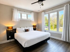 Ein Schlafzimmer mit Bett, Nachttischen, Deckenventilator und großen Fenstern.