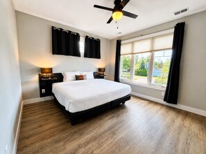 A bedroom with a bed, two bedside tables, a ceiling fan, a window with curtains, and a view of the outside. - The Haven 10 | 2BR | Rooftop Patio |Downtown (Traverse City)