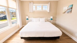 Ein Schlafzimmer mit einem großen Bett, zwei Nachttischen, einem Fenster mit Vorhängen und einem Bild an der Wand.