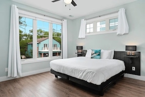 Ein Schlafzimmer mit einem großen Bett, zwei Nachttischen, einem Deckenventilator und Blick auf ein Haus durch ein Fenster.