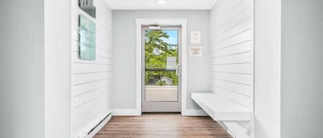 A narrow hallway with wooden flooring, white walls, and a door leading outside.