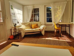 Ein Wohnzimmer mit einer Couch, einem gelben Sessel, einem Tisch und einem großen Fenster mit Vorhängen.