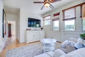 Ein Wohnzimmer mit Deckenventilator, Flachbildfernseher, weißen Schränken und einem runden Couchtisch.