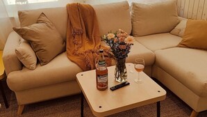 Ein beiges Sofa mit Decke, eine Flasche Alkohol, eine Vase mit Blumen und ein Glas auf einem kleinen Tisch.
