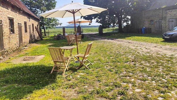 Ein rustikaler Außenbereich mit einem Backsteinhaus, einem Tisch mit Stühlen und einem großen Sonnenschirm.