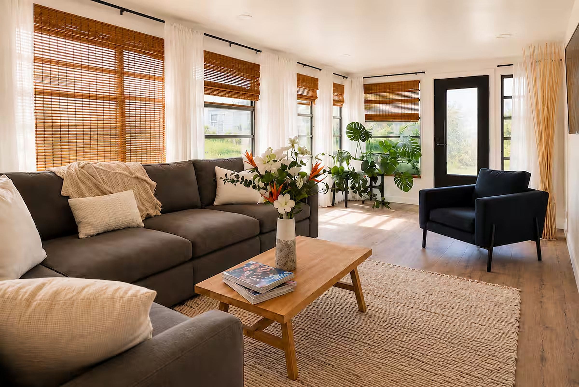 A modern living room with a brown sofa, a coffee table with magazines, and a black armchair.