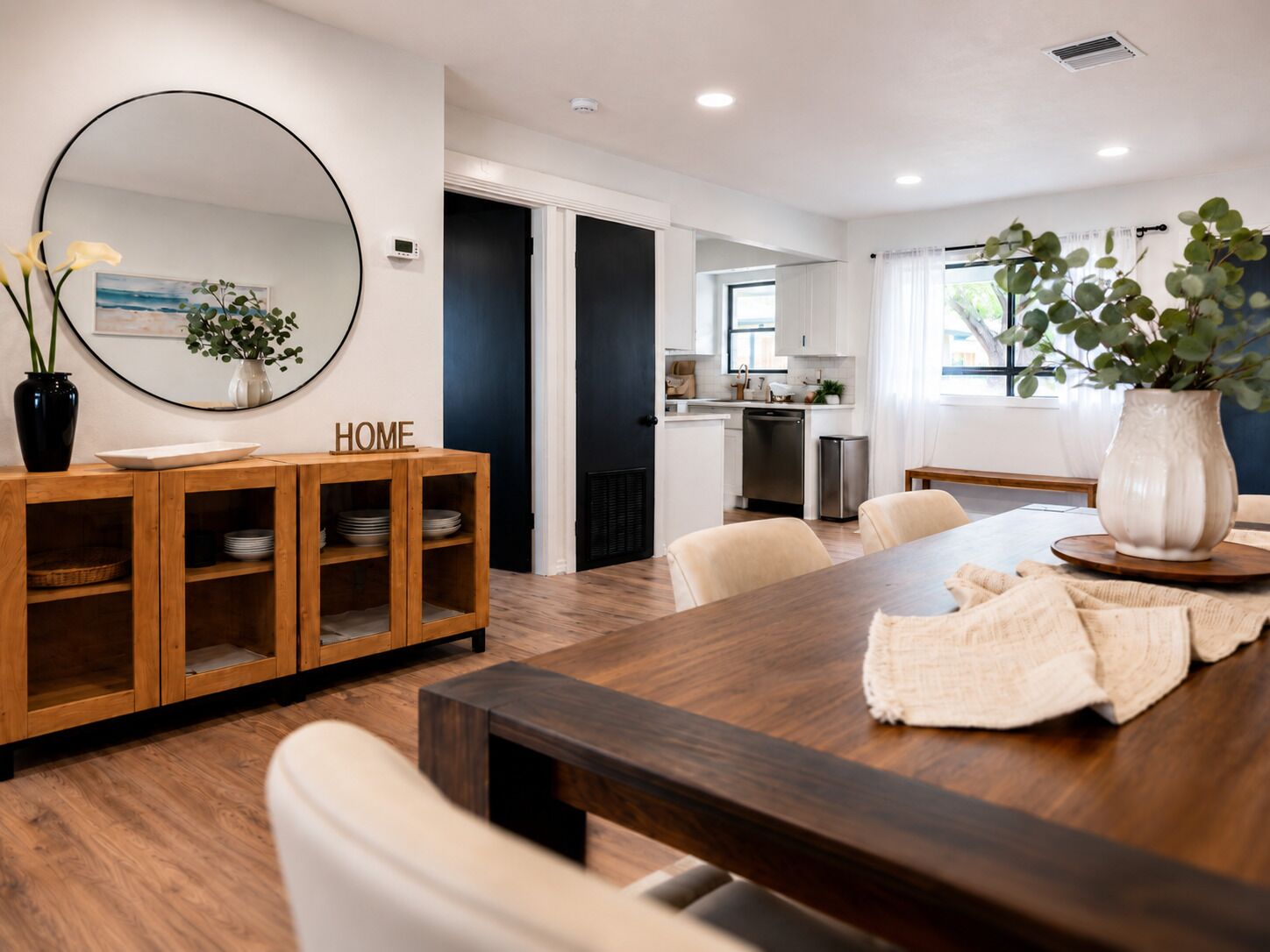 Un comedor moderno con una mesa de madera, sillas, un espejo y un jarrón con flores.