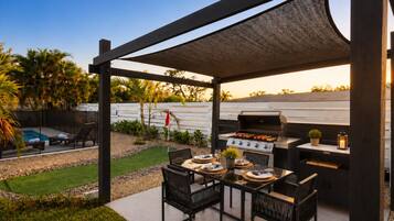 Un patio exterior con una parrilla, asientos y una piscina.