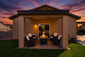 A covered patio with two chairs and a table, a fire feature, and a view of the sunset. - Luxury Private Pool & Spa Home | Resort Backyard | Sleeps 10 (Tucson)