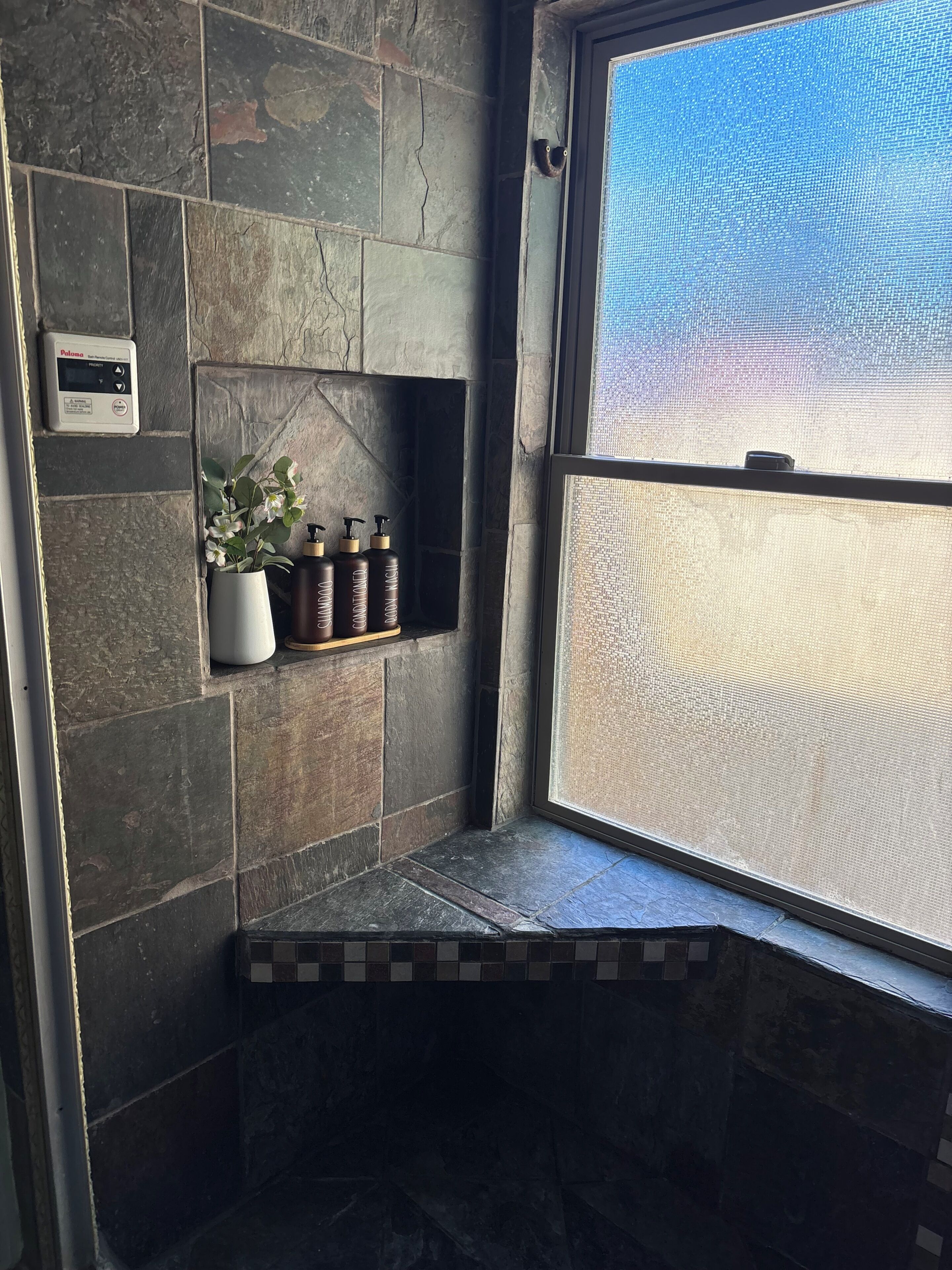 A stone-walled bathroom with a built-in bench, a window with a view, and a thermostat on the wall.