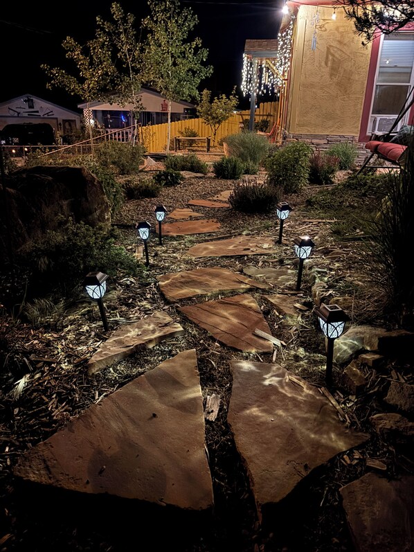 Caminho iluminado em um jardim noturno, com lajes de pedra e lanternas decorativas.